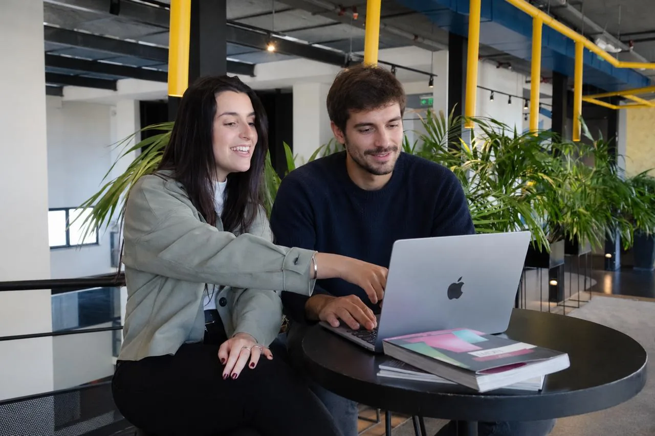 Dos personas revisando juntas un trabajo en la computadora en una oficina